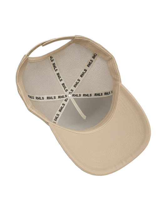 Interior look at the RWLS creamy beige color snapback trucker hat with mesh side panels. Black RWLS logo branding on the inseam tape. Dual snap strap. rebelliouswealth.com